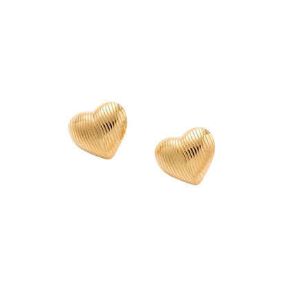 Gold heart-shaped stud earrings with parallel ridged texture on cream background