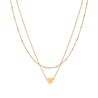 Delicate double-chain gold necklace with tiny heart pendant on cream background