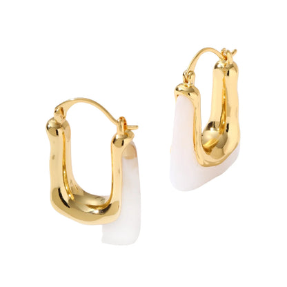 Sculptural gold-plated hoop earrings with flowing curved design and lever-back closure on cream background.