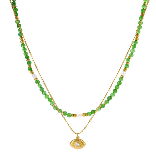 Layered necklace with green stone beads, gold spacers, white accents, and protective eye pendant on cream background.