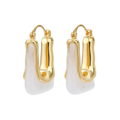 Sculptural gold-plated hoop earrings with flowing curved design and lever-back closure on cream background.
